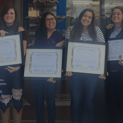 Four women proudly holding certificates and smiling.