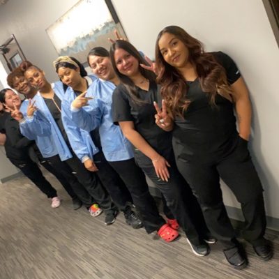 A group of seven people posing indoors, smiling and making peace signs.
